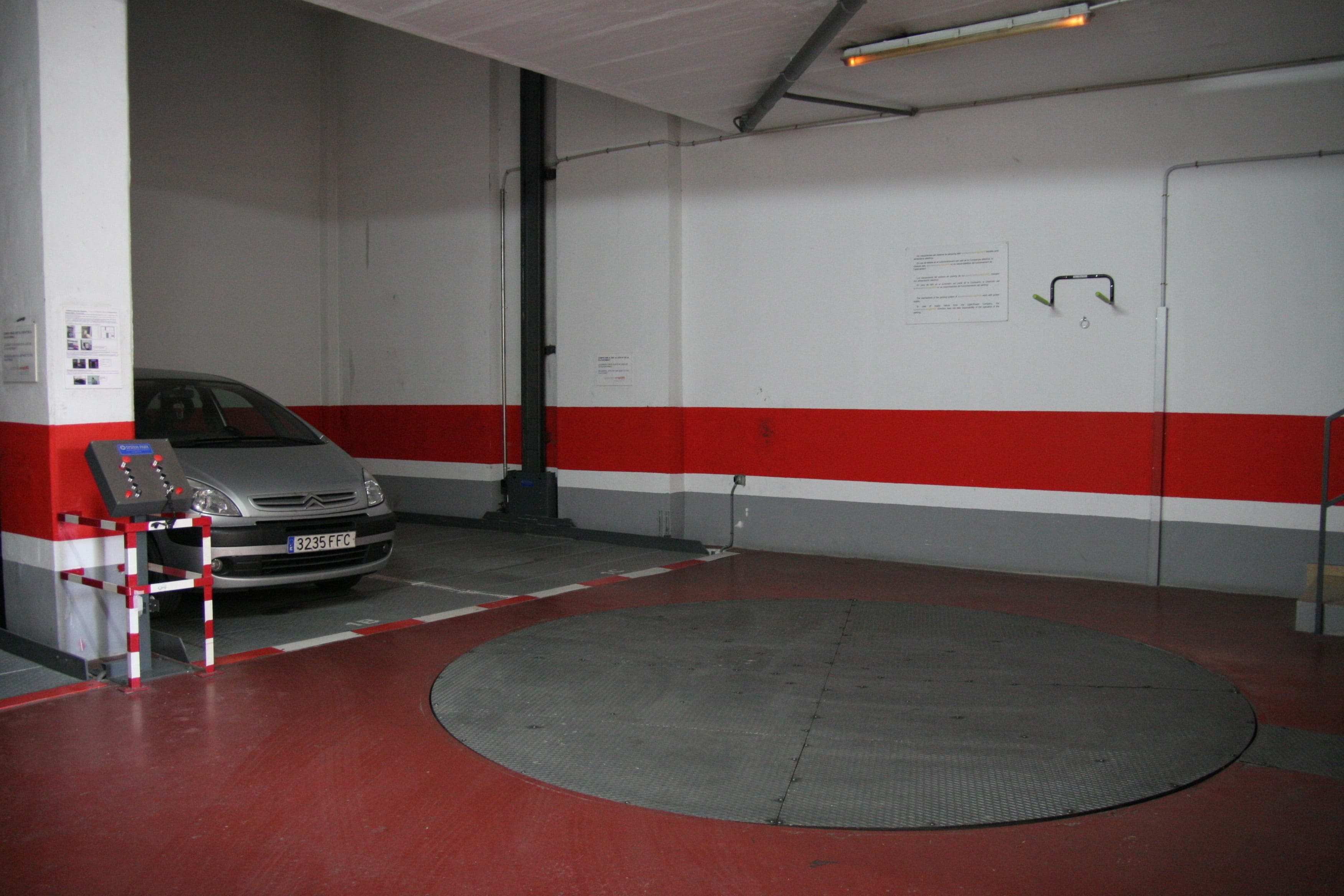 A parking garage with a red and white color scheme, a car parked near a control panel, and a circular mat in the center.