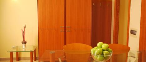 Un comedor moderno con una mesa de vidrio, dos sillas anaranjadas, un armario de madera y un bol con manzanas verdes.