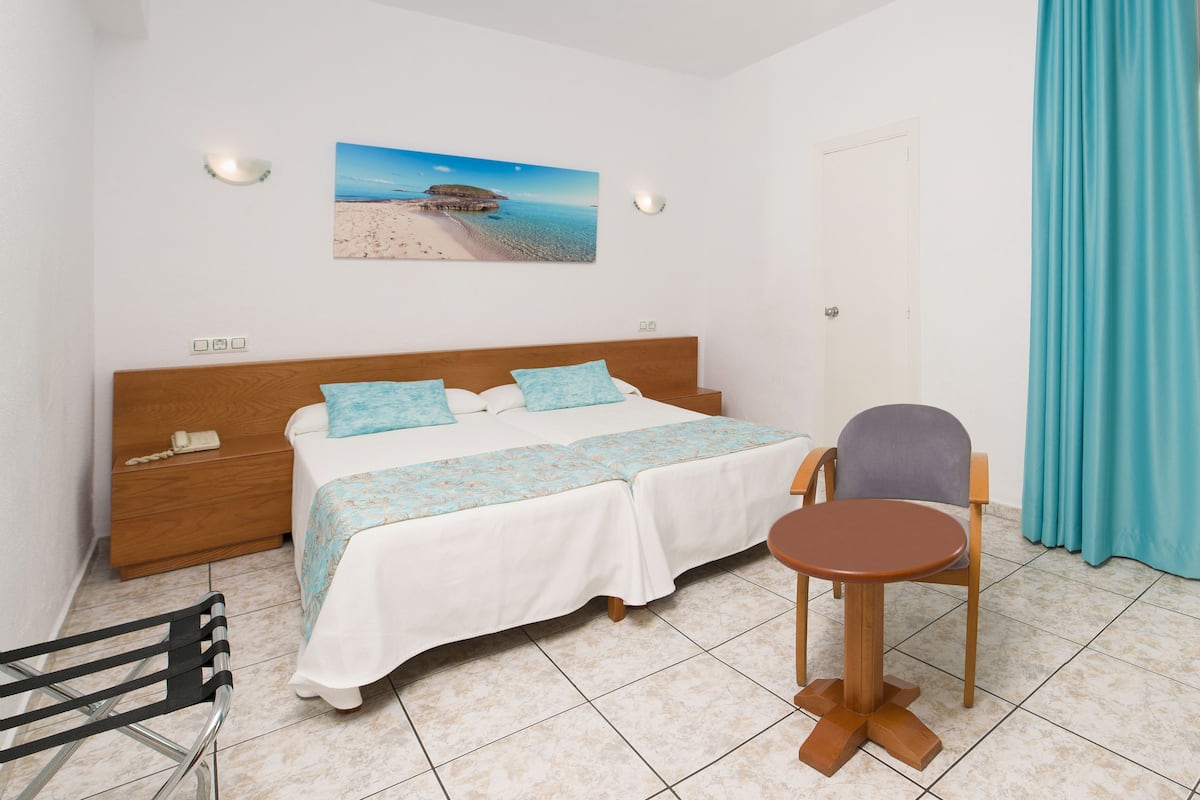 Quarto com cama, mesas de cabeceira, uma cadeira, uma mesinha e um quadro na parede.