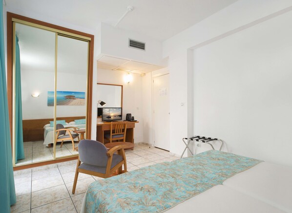 Una habitación de hotel con una cama, un escritorio con una computadora, una silla y una mesita.