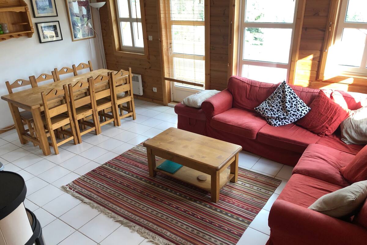 A cozy living room with a wooden dining table, red sofa, and a patterned rug.
