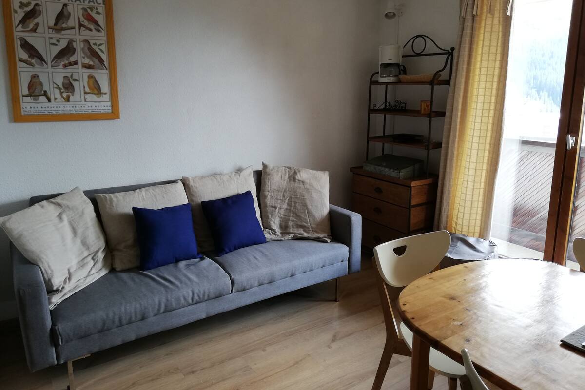 A living room with a grey sofa, blue cushions, a wooden coffee table, and a framed poster on the wall.