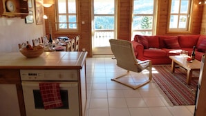 Een gezellig houten chalet interieur met een eethoek, een rode bank en uitzicht op bergen door grote ramen.
