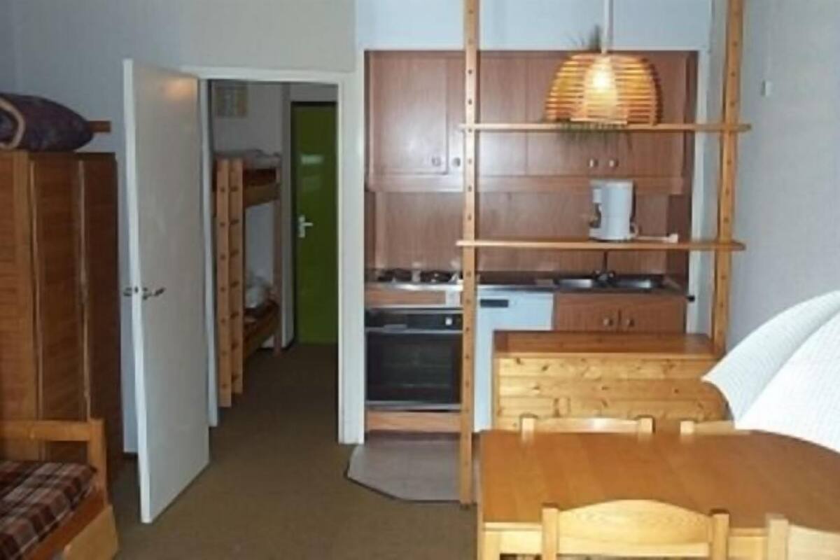A compact room with a kitchenette, a wooden dining table, and a bench.