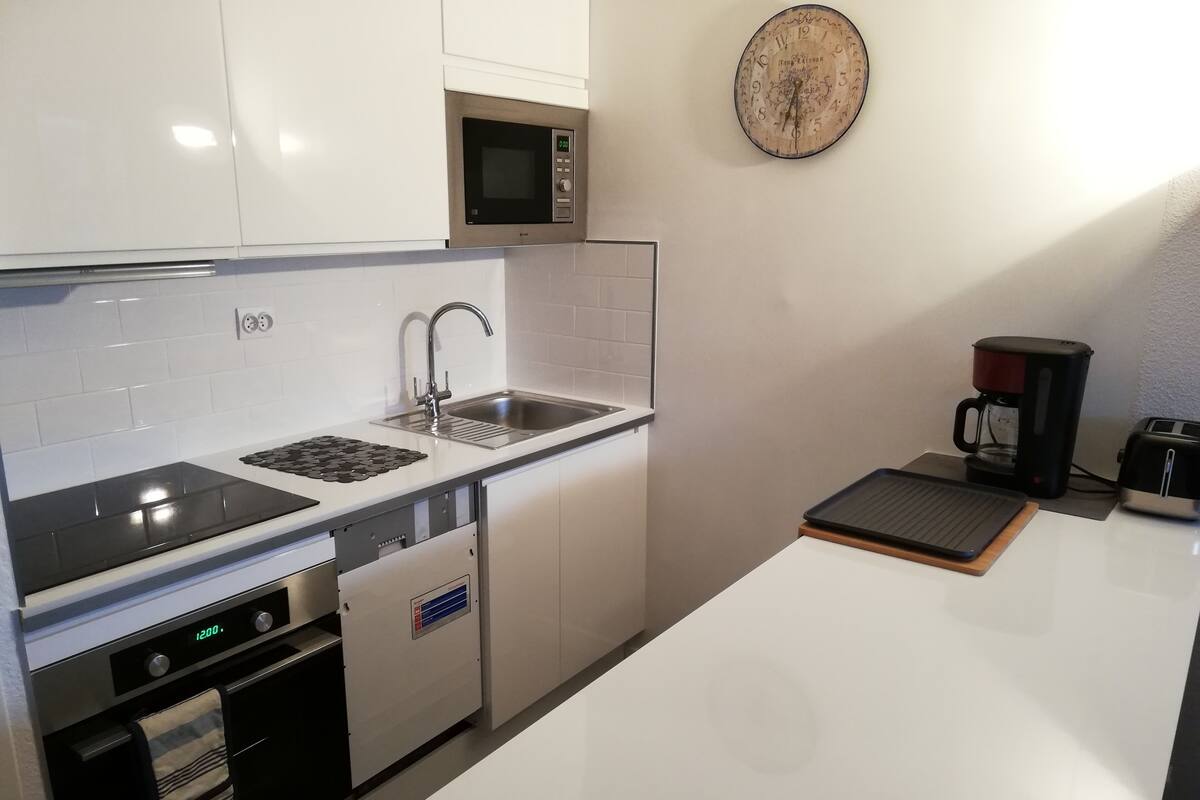 A modern kitchen with white cabinets, a stainless steel sink, a microwave, an oven, and a coffee maker.