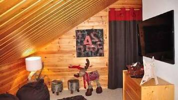 Cozy cabin-style room with a sloped ceiling, featuring a mounted TV and a rustic charm.