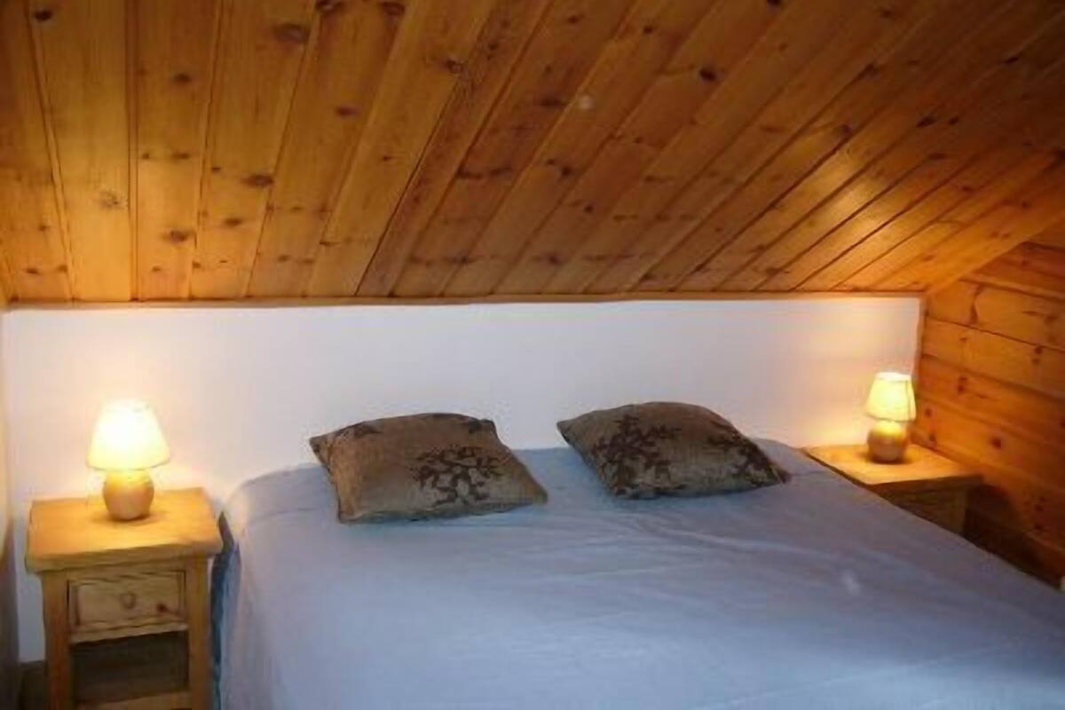 A room with a wooden ceiling, a bed with white bedding, two decorative pillows, and two bedside lamps.