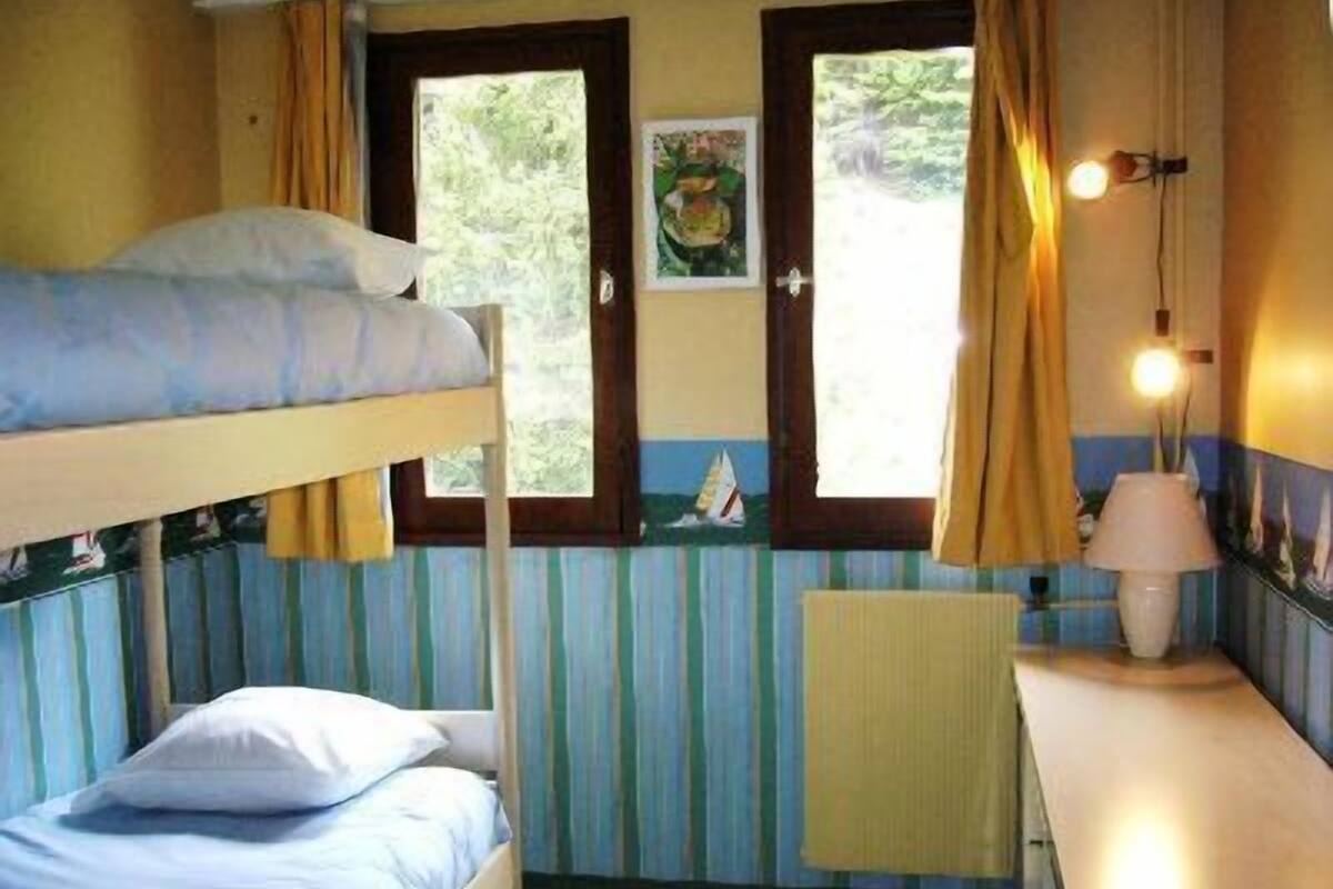 A room with bunk beds, a window with curtains, a painting, a lamp, and a small table.