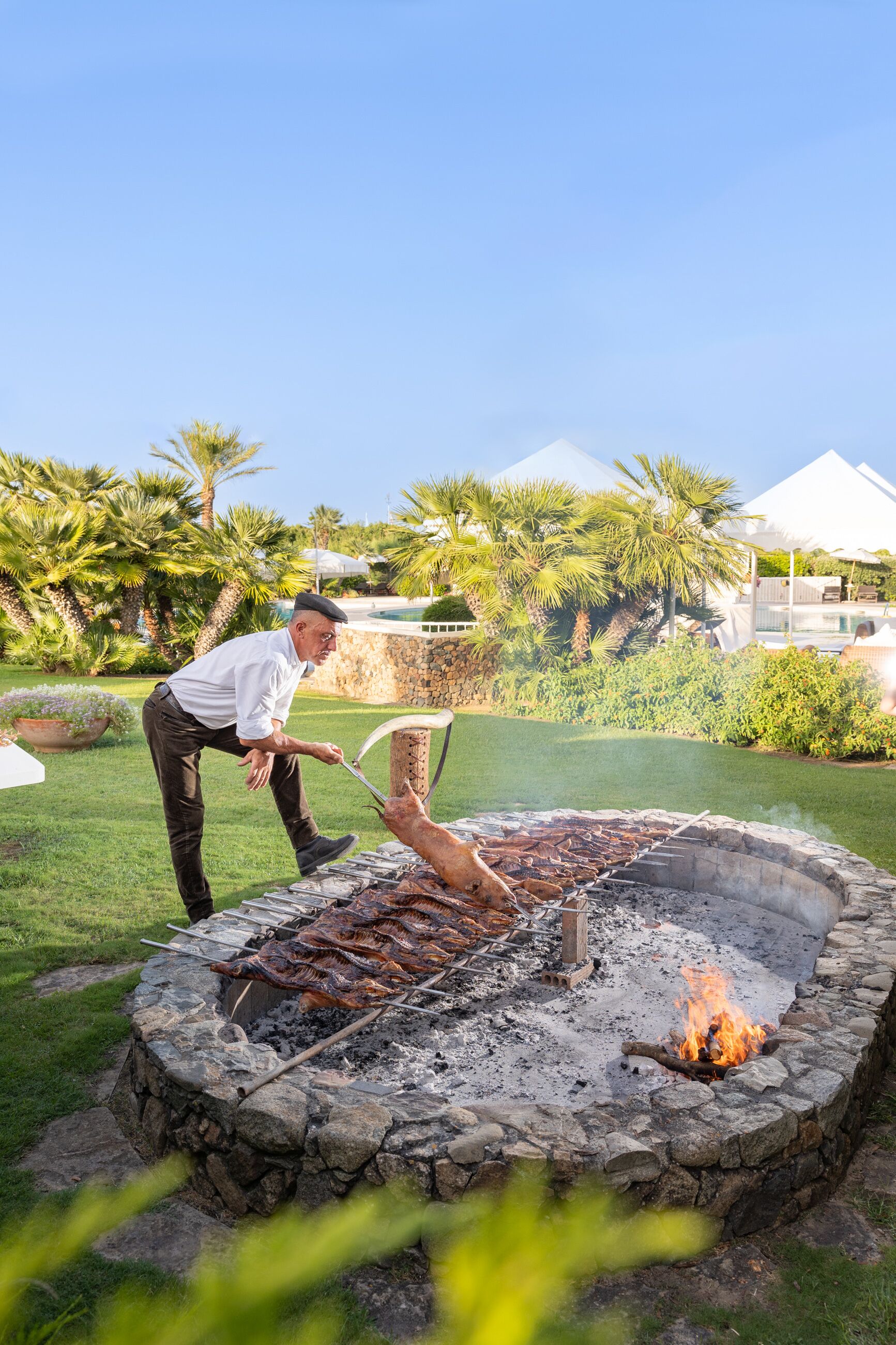 A stone fire pit with a grill, surrounded by a stone wall and greenery.
