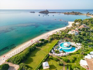 An aerial view of a coastal resort with a beach, a swimming pool, and a fortified structure in the background. - Hotel Baia di Nora (Pula)