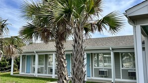 A building with a light blue exterior, a covered porch, and a well-maintained lawn with two palm trees. - Oceanview Inn (Emerald Isle)