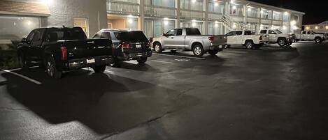 A parking lot with several parked vehicles in front of a building with multiple balconies and a large garage door.