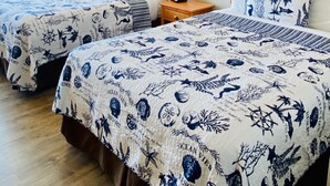 A hotel room with two beds, each with a nautical-themed bedspread. There is a wooden headboard, a nightstand with a phone, and a window with curtains. - Oceanview Inn (Emerald Isle)