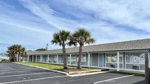 A motel with a parking lot, palm trees, and a clear sky. - Oceanview Inn (Emerald Isle)
