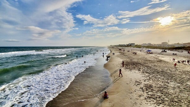 A beach with waves, people, and buildings in the background. - Oceanview Inn (Emerald Isle)