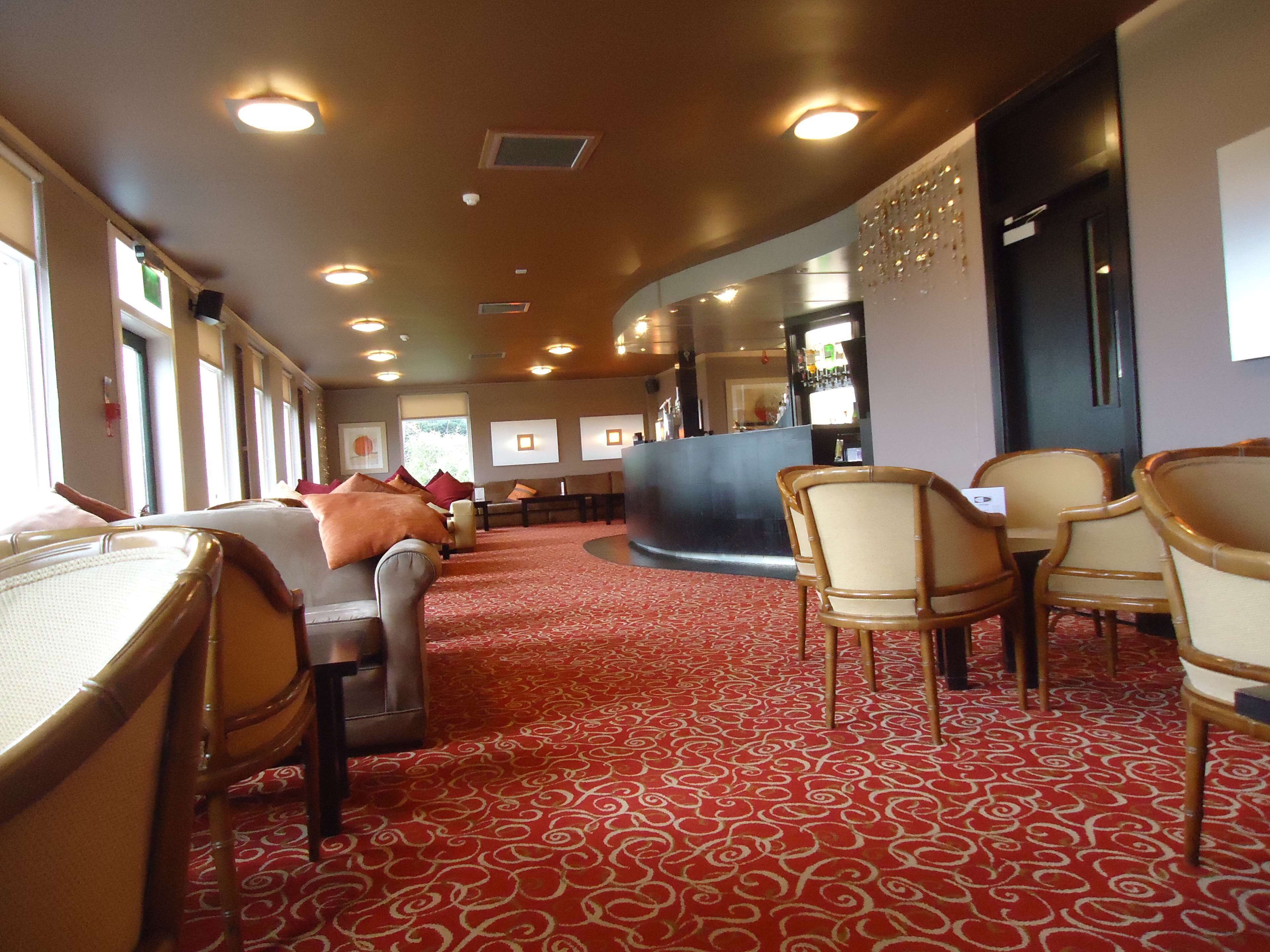 Un hall d’hôtel avec un tapis rouge à motifs, un espace salon avec des fauteuils et des canapés, un comptoir de réception et un bar.