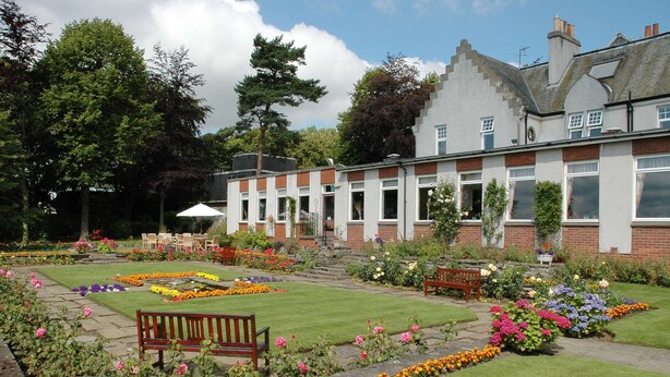 A garden with a bench, a building with a brick facade, and a lawn.