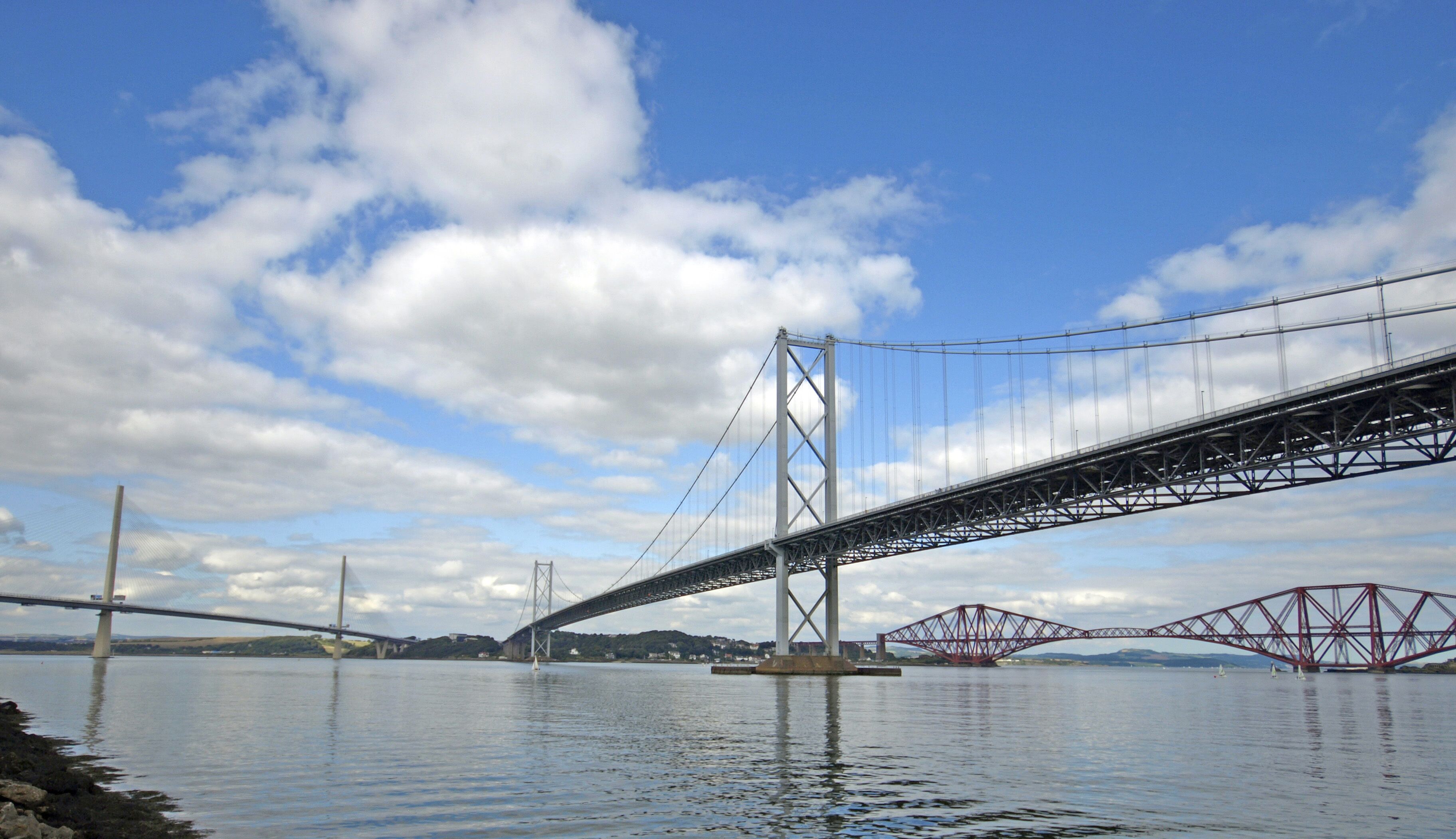 Un gran puente colgante sobre un cuerpo de agua, con cielo despejado y algunas nubes.