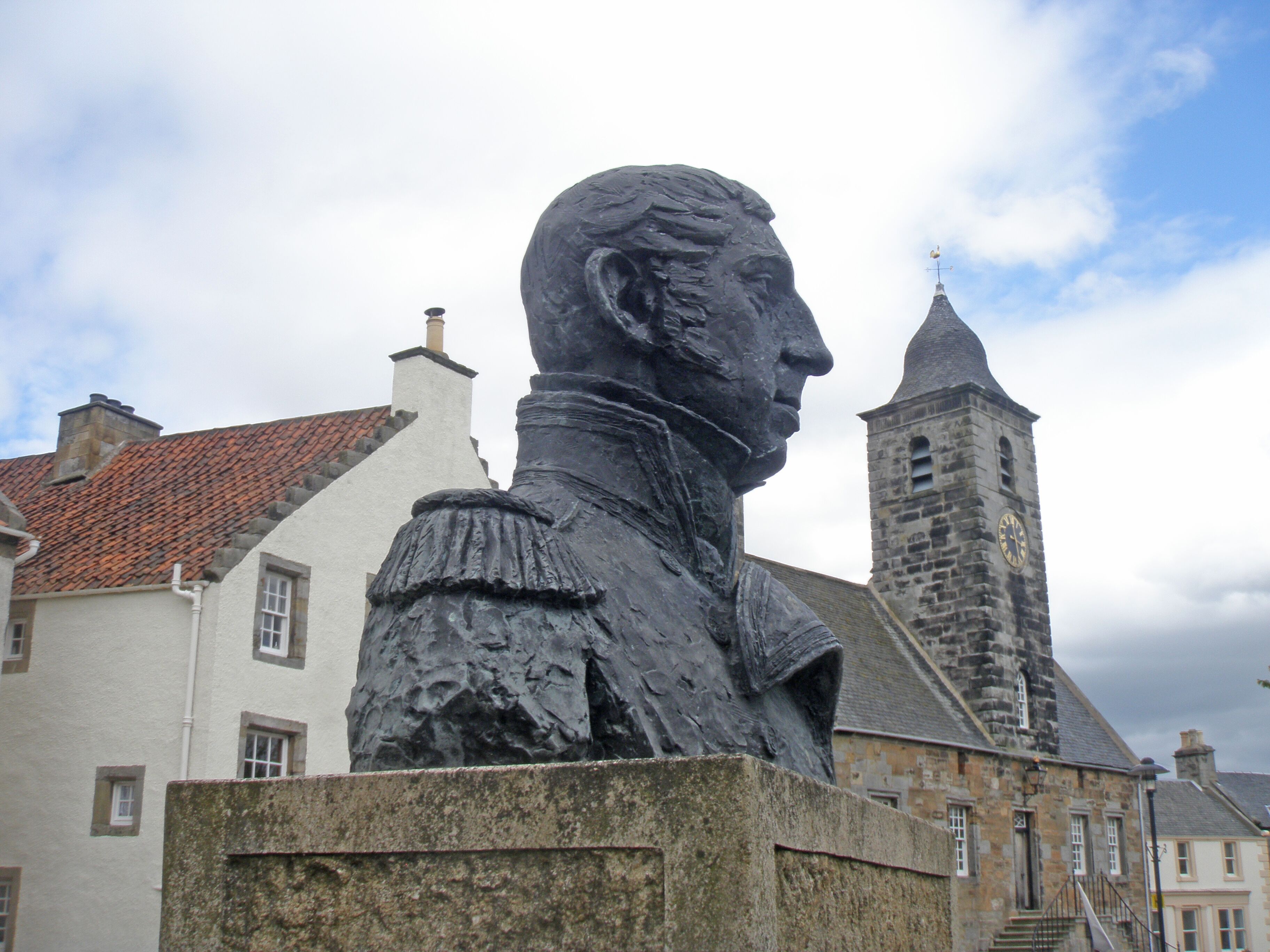 A statue of a historical figure in a public square, with traditional buildings in the background.