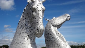A large metallic sculpture of two horses with a grassy field and a clear sky in the background.