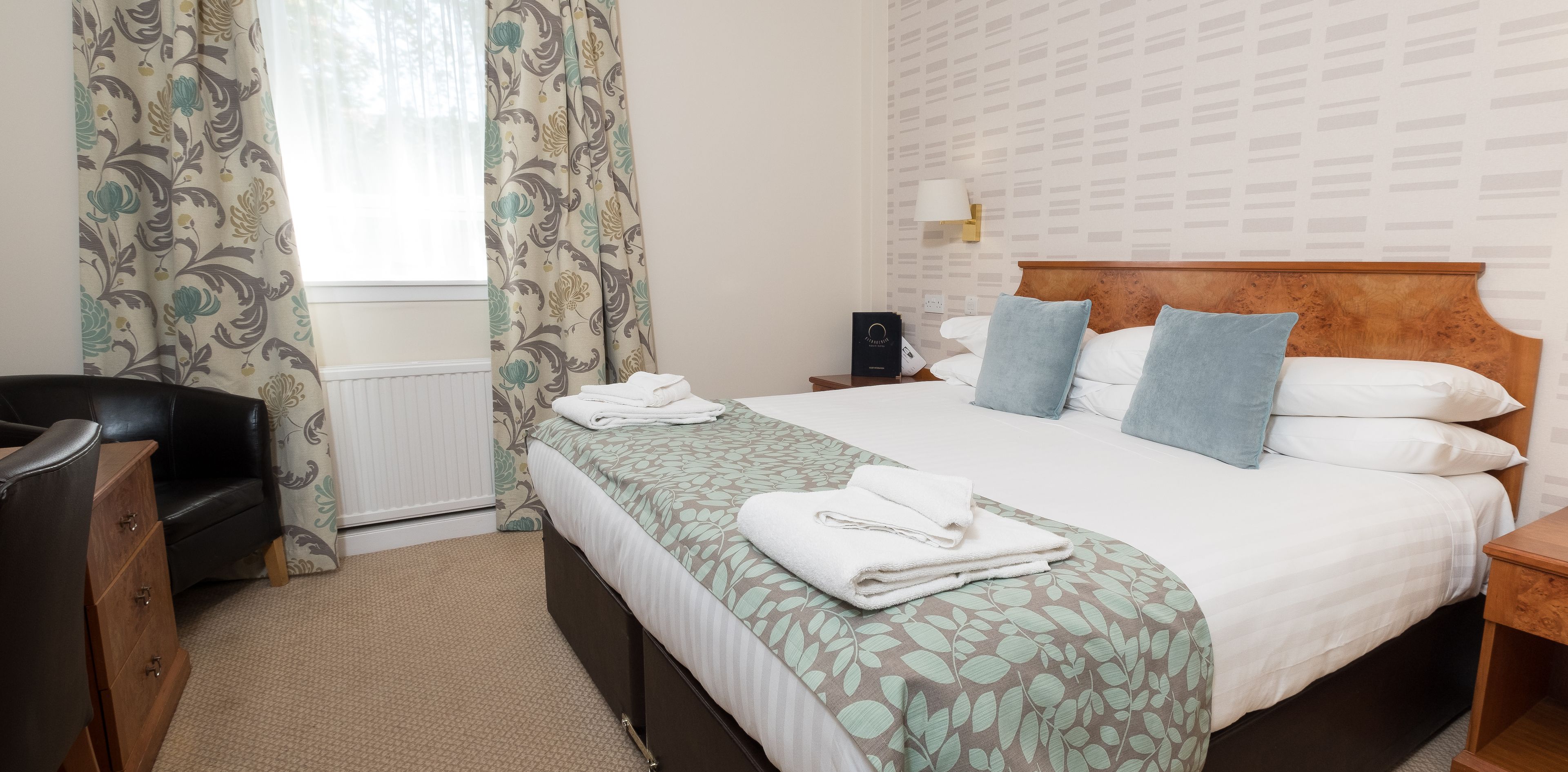 A neatly arranged hotel room with a bed, bedside table, lamp, and a chair.