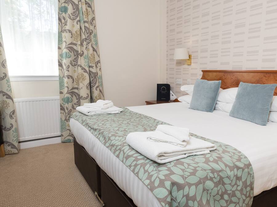 A neatly arranged hotel room with a bed, bedside table, lamp, and a chair.