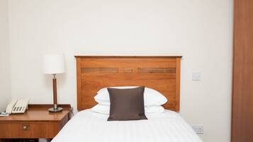 A hotel room with a wooden headboard, a bedside table with a lamp, a phone, and neatly made bed with white and brown pillows.