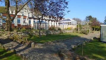 A residential area with a stone pathway, a bench, and a garden with a variety of plants and flowers.