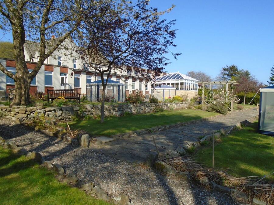 A residential area with a stone pathway, a bench, and a garden with a variety of plants and flowers.