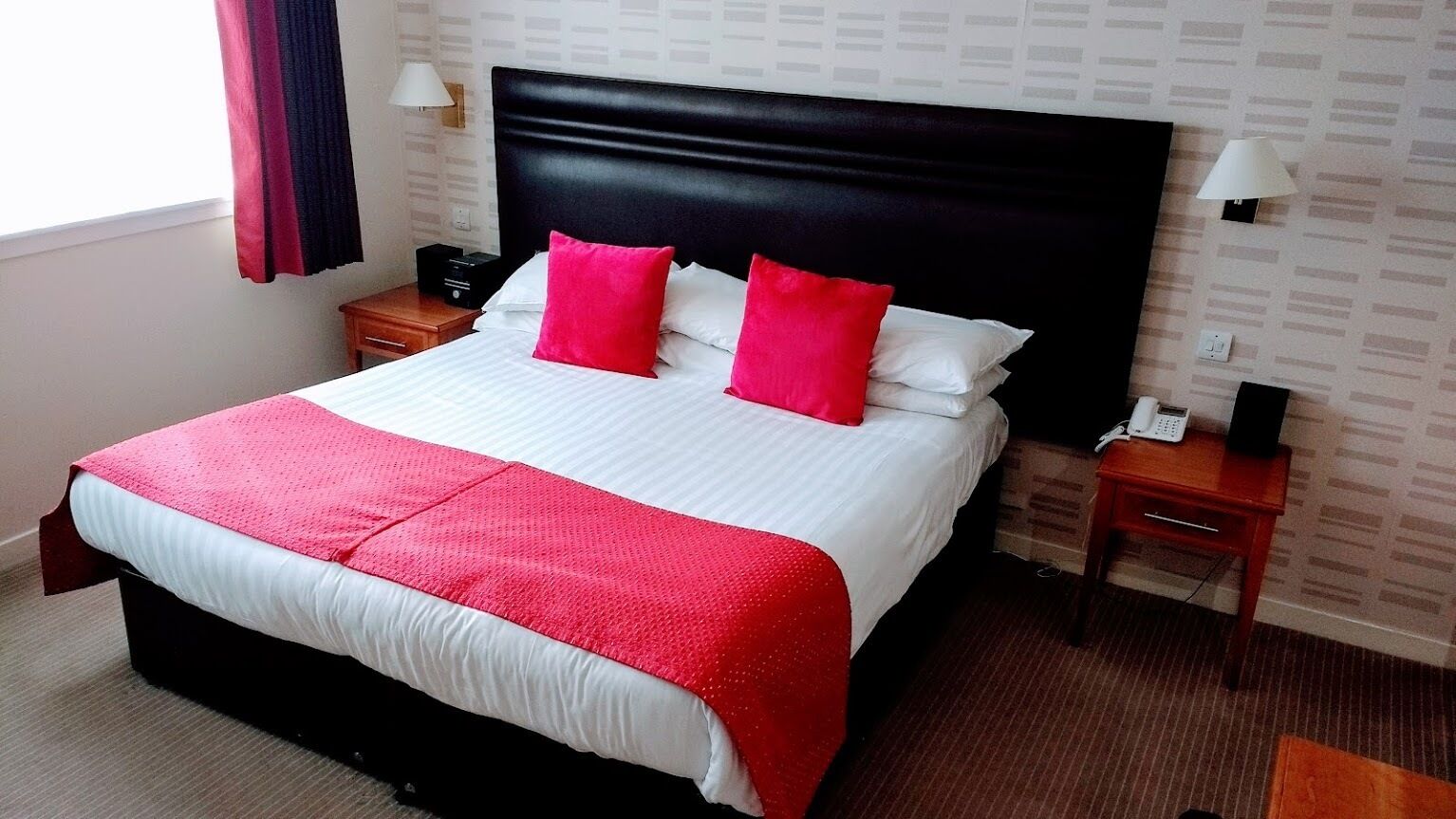 A hotel room with a large bed, two bedside tables, a nightstand, a lamp, and a telephone.