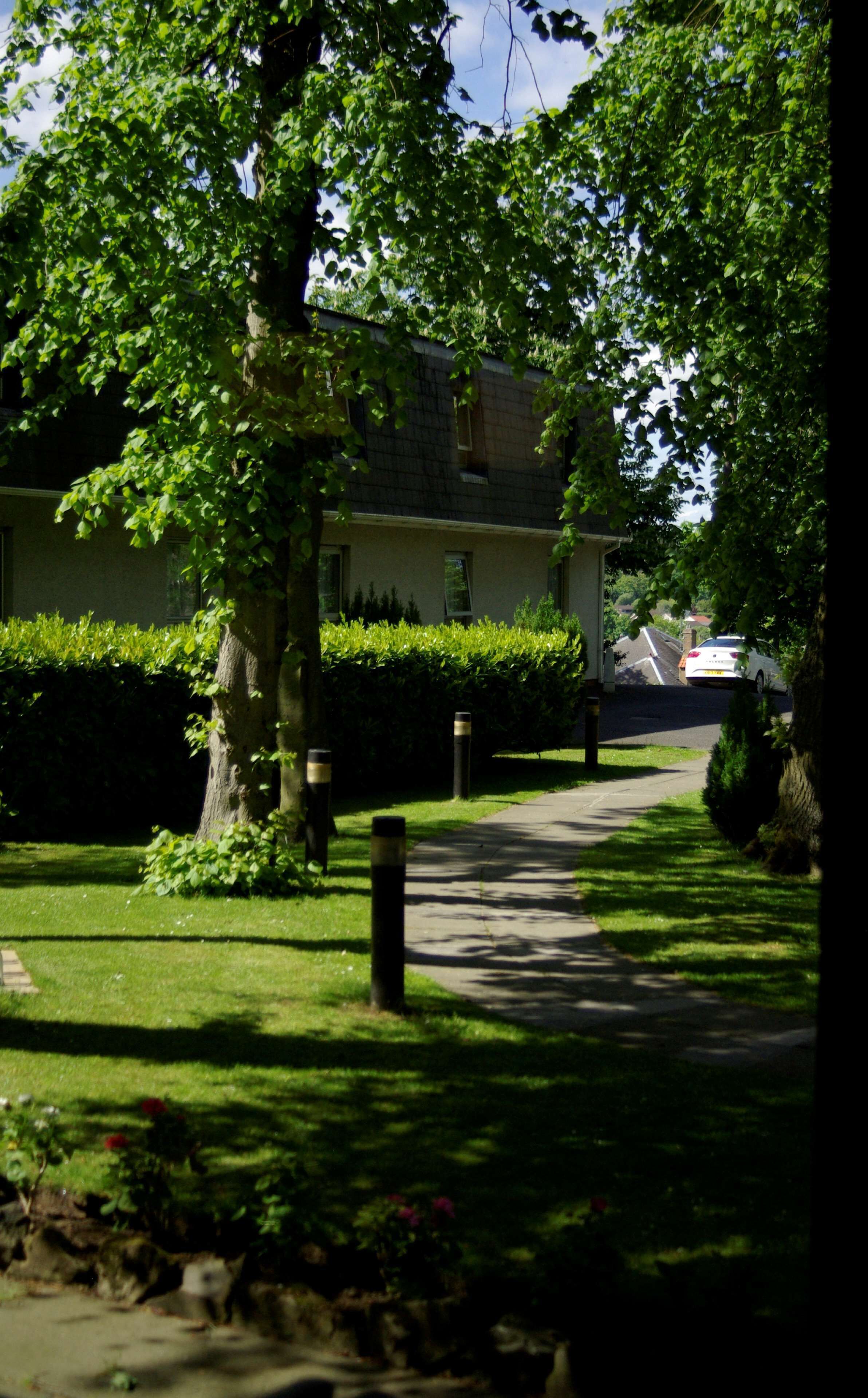 A residential street with a house, a sidewalk, and a car parked on the street.