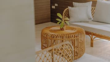 A wicker ottoman with a plant on top, a white sofa with cushions, and a wooden headboard in a hotel room.
