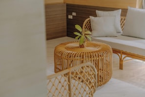 Un reposapiés de mimbre con una planta encima, un sofá blanco con cojines y un cabecero de madera en una habitación de hotel.