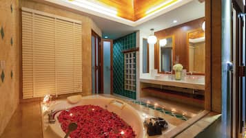 A modern bathroom with a large bathtub filled with rose petals, a vanity with a mirror, and a shower area.