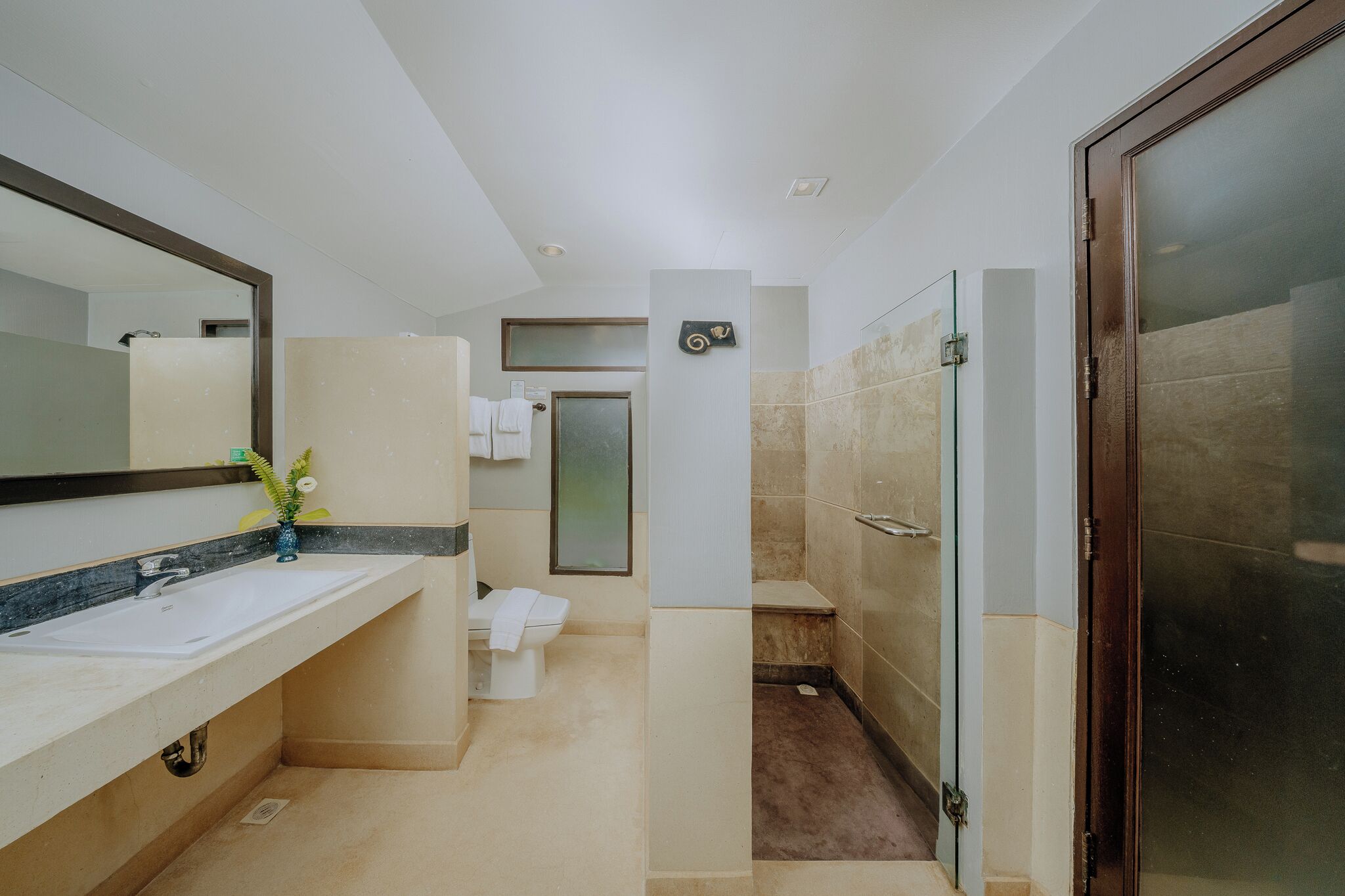 Un baño moderno con un espejo grande, un lavamanos, un inodoro y una zona de ducha.