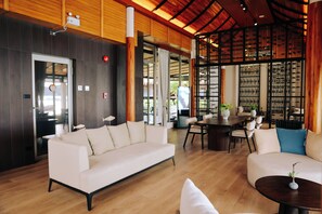 A modern interior with a wooden ceiling, a white sofa, a dining table, and a view through a glass door. - Railay Bay Resort and Spa (Krabi)