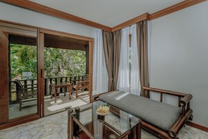 Een kamer met een bed, een glazen tafel met een mand, en uitzicht op een balkon met stoelen.