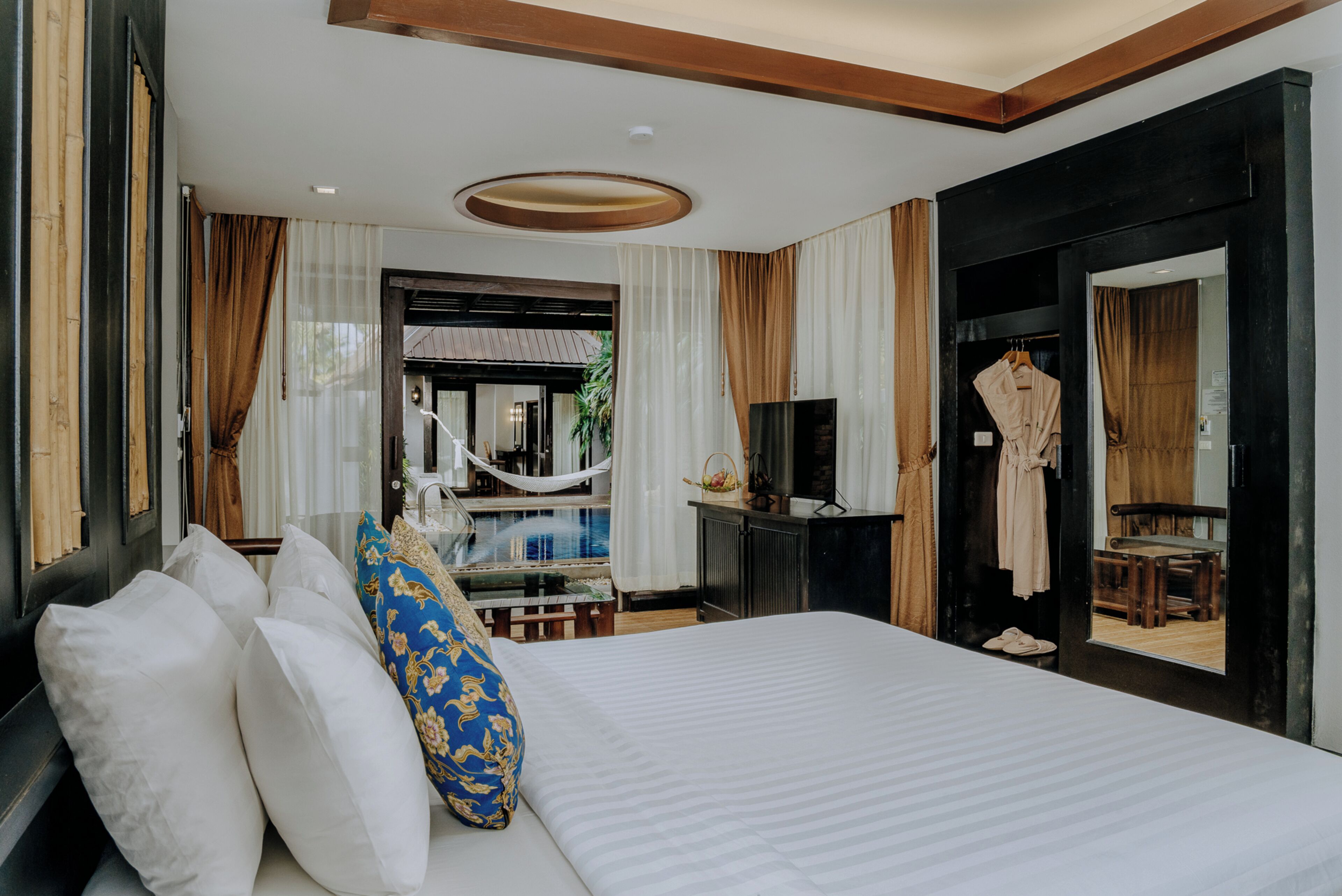 Een hotelkamer met een groot bed, een televisie, een bureau en uitzicht op een buitenzwembad.