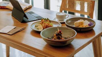 A wooden table with a laptop, a cup, and bowls of food.