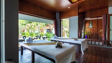 A spa room with two massage tables, a bench, and a view of the garden.