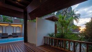 A wooden deck with a pool, lounge chairs, and a view of a tropical landscape with a sunset. - Railay Bay Resort and Spa (Krabi)