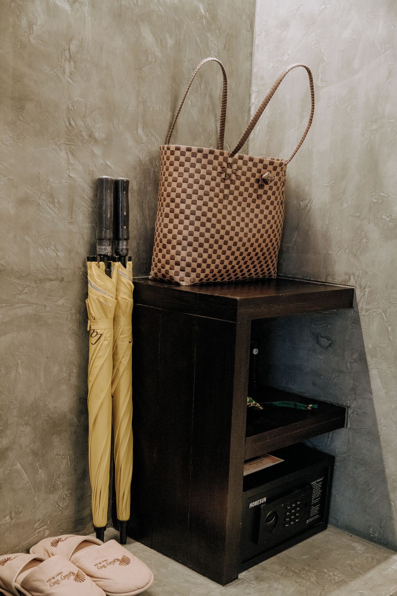 Un mueble de madera oscura con un bolso de cuadros encima, un paraguas amarillo y unas zapatillas.