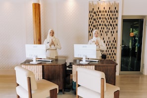 Zona de recepción con dos recepcionistas, un mostrador de madera y dos monitores de computadora.