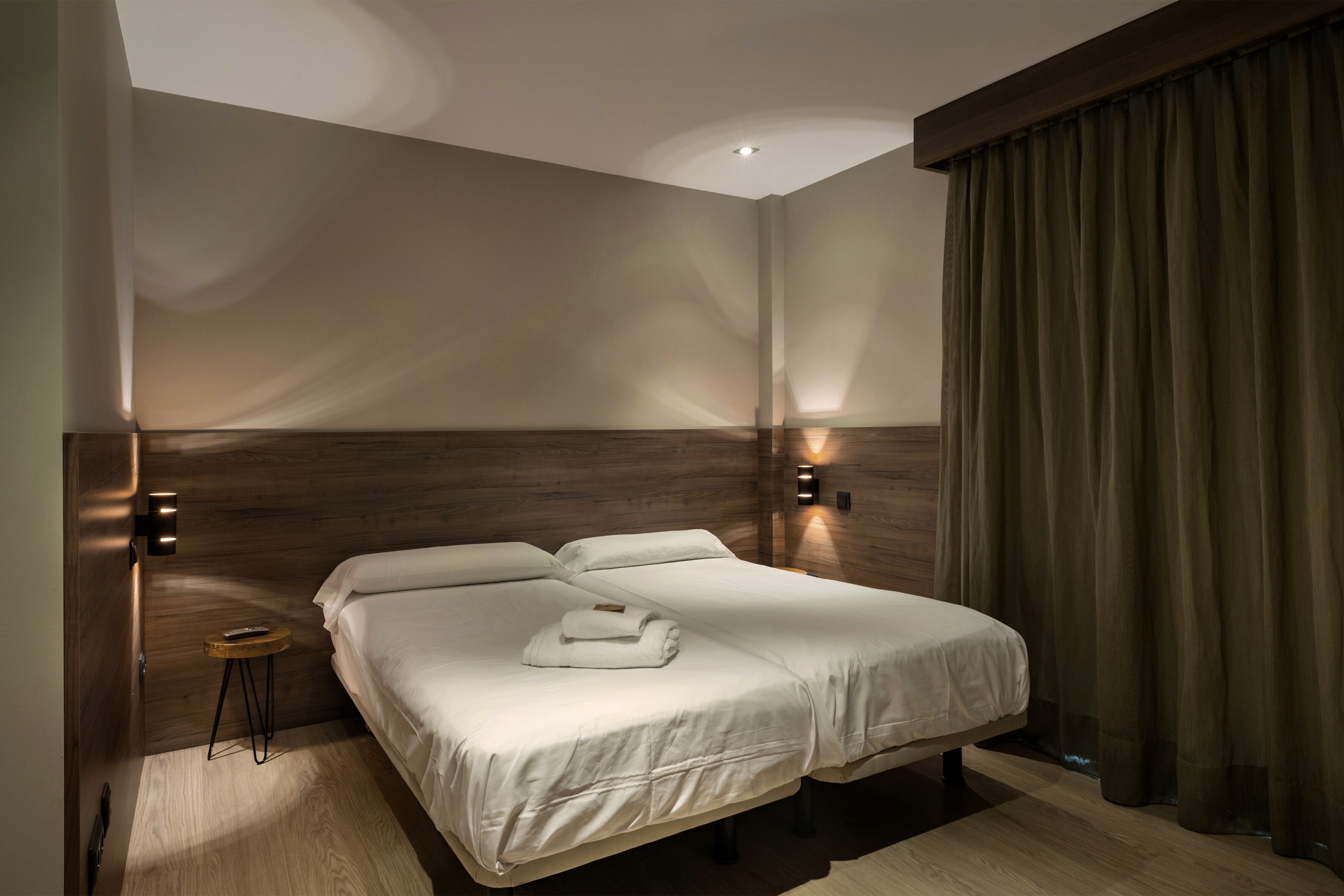 A modern hotel room with a large bed, a small side table, and a wall-mounted light fixture.