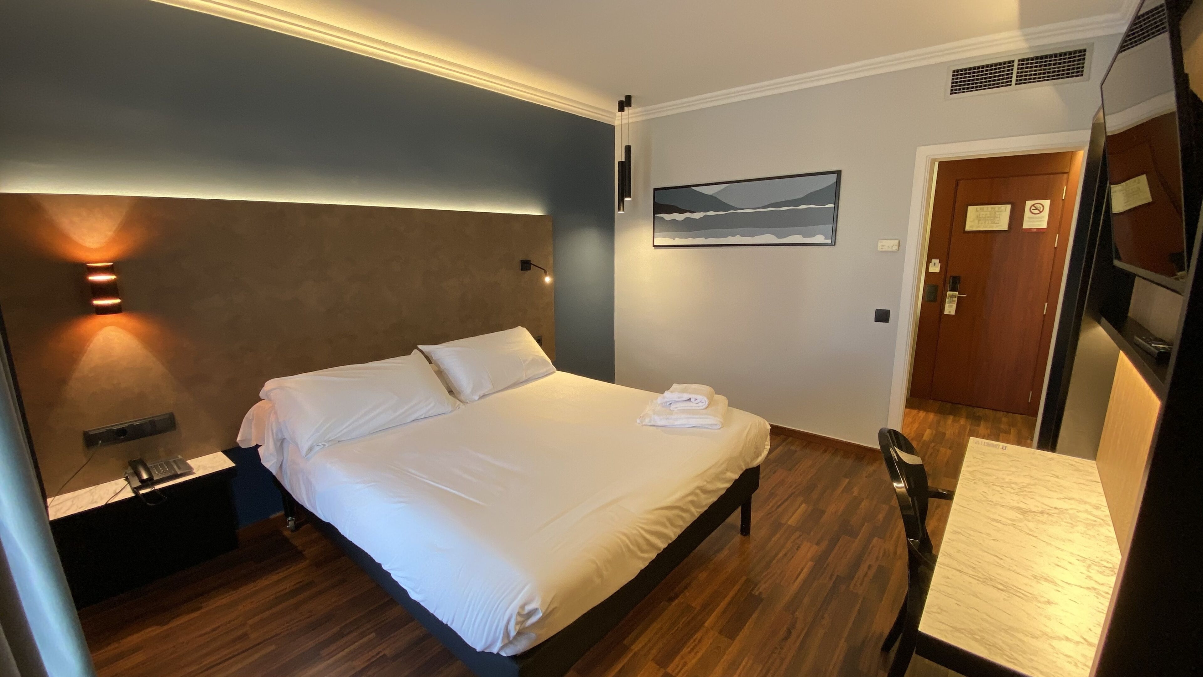 Una habitación de hotel con cama, mesita de noche y escritorio.