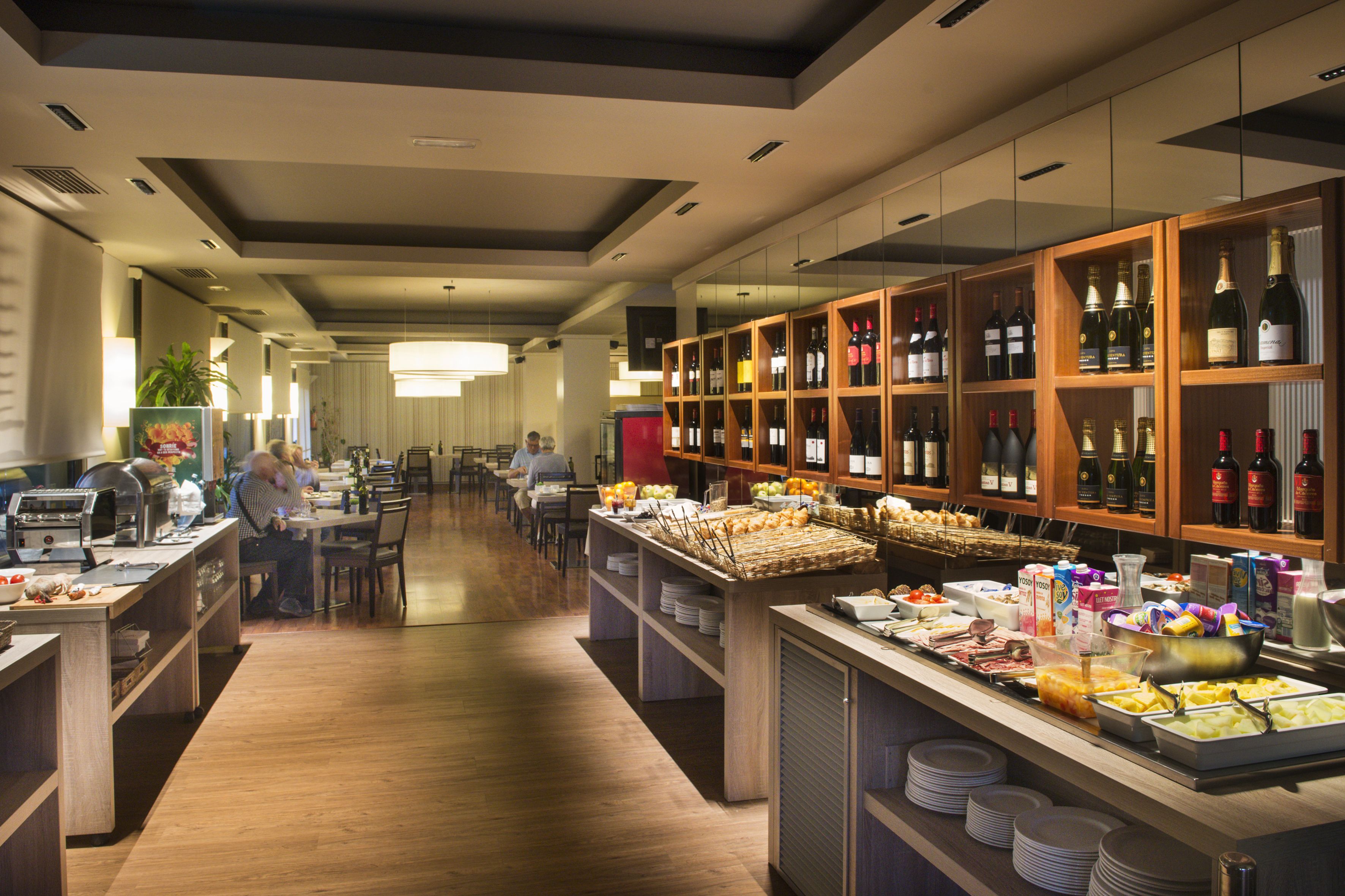 Een ontbijtruimte van een hotel met een buffet, een wijnassortiment en zitplaatsen voor gasten.