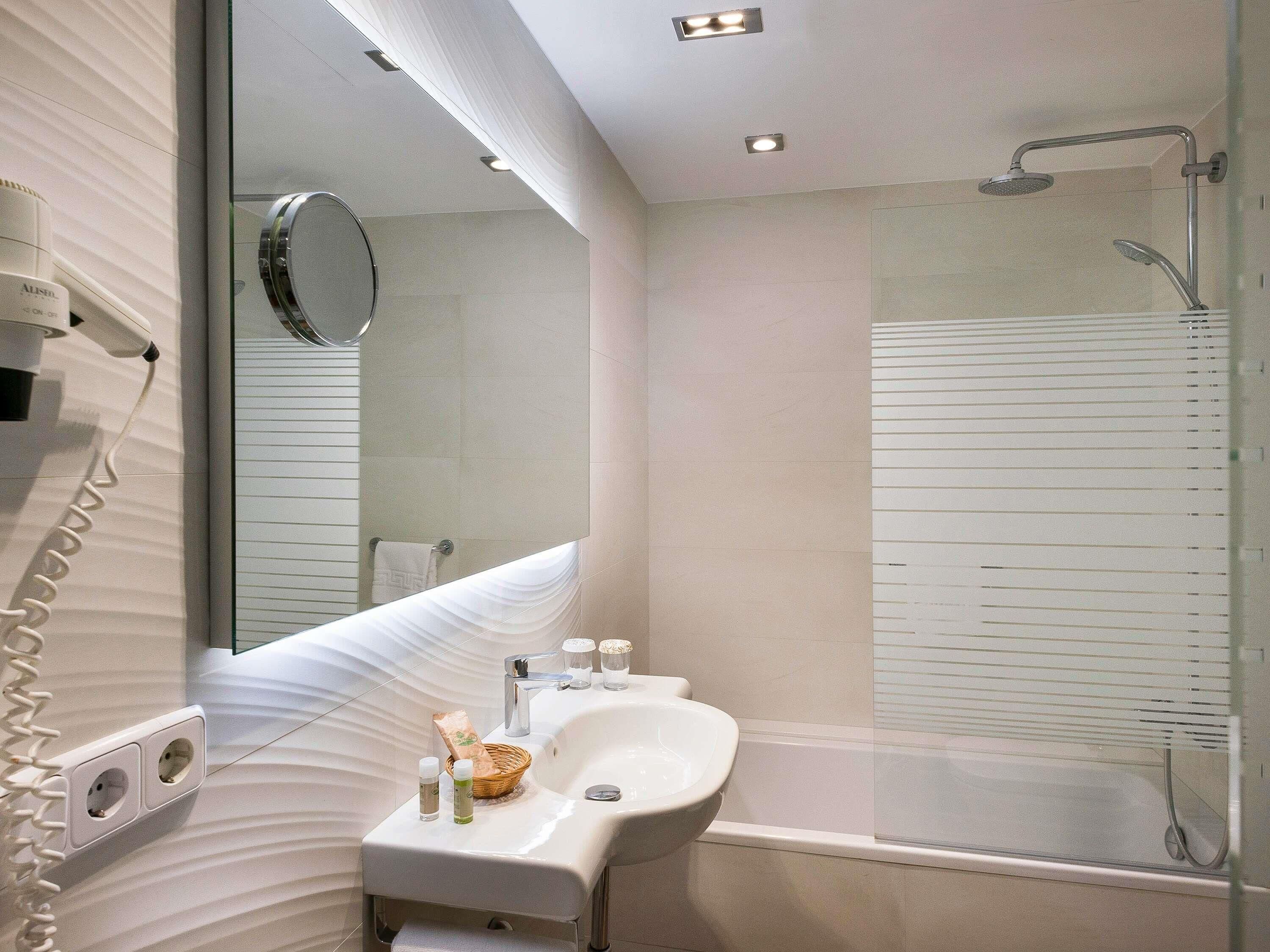A modern bathroom with a glass shower enclosure, a white sink with a mirror, and a towel rack.