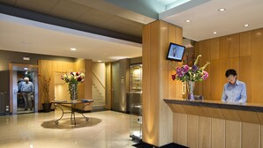 Zona de recepció d'hotel amb un taulell de fusta, un televisor penjat a sobre i un ram de flors.