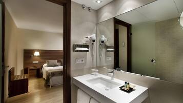 Une salle de bain d’hôtel moderne, dotée d’un grand miroir, d’un lavabo blanc et d’un sèche-cheveux fixé au mur.