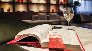 Un libro abierto sobre una mesa con una copa de vino blanco, un separador rojo y una estantería al fondo.